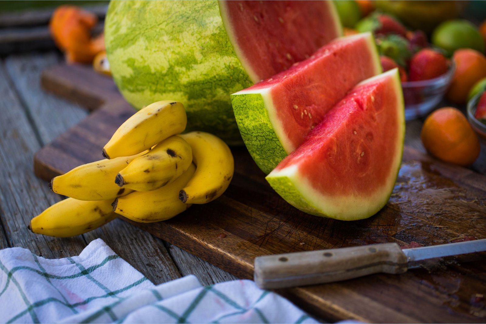 Kaliumrike bananer ligger ved siden av en L-citrullinrik, oppskåret vannmelon på et skjærebrett